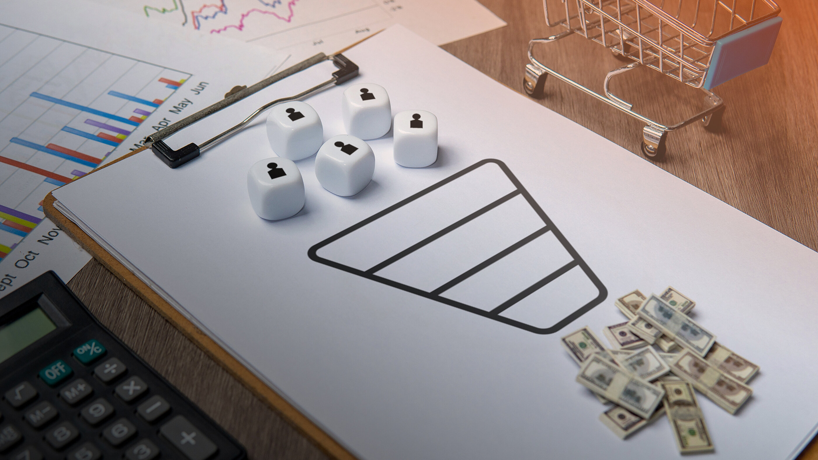 Vertriebsfunnel mit Kundensymbolen, Einkaufswagen, Geldscheinen und Diagrammen auf einem Schreibtisch
