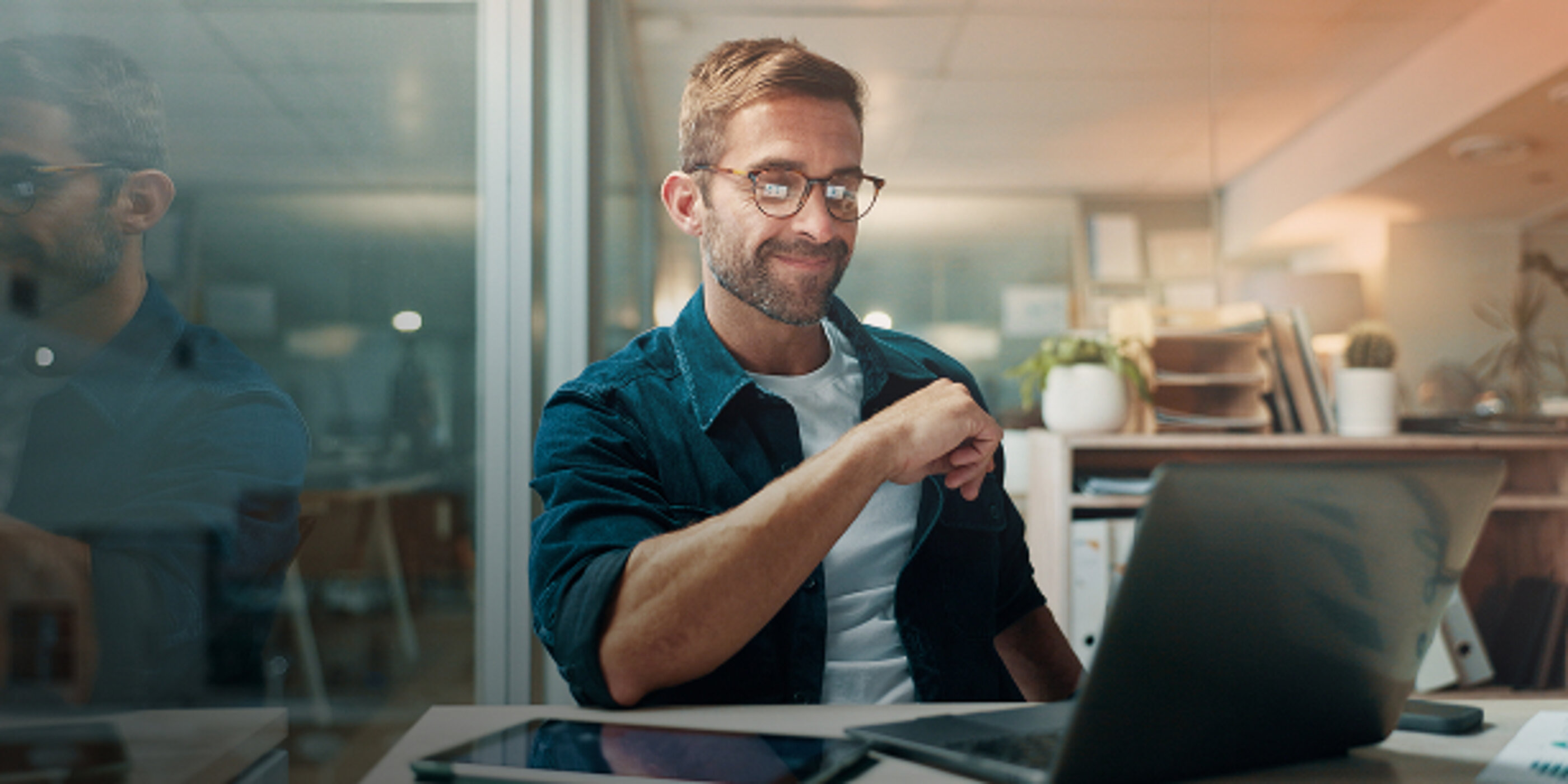 Mann mit Brille am Schreibtisch vor einem Laptop in modernem Büro